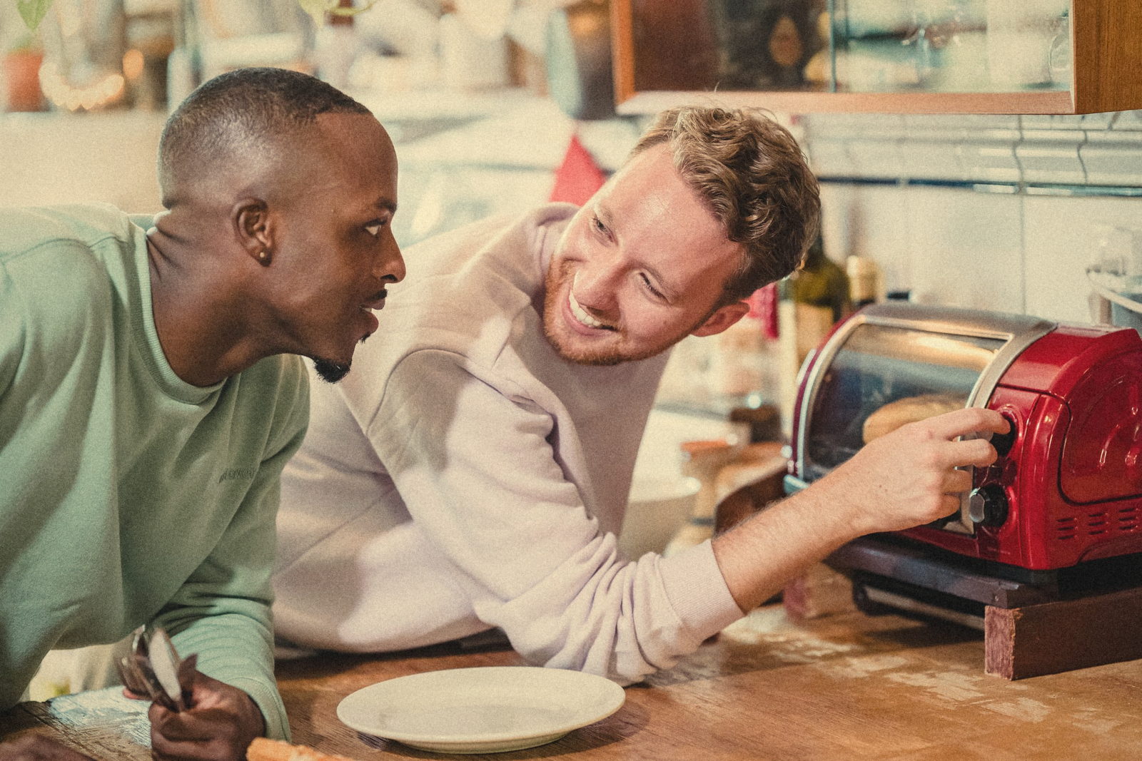 Two friends laughing over the toaster in a shared kitchen