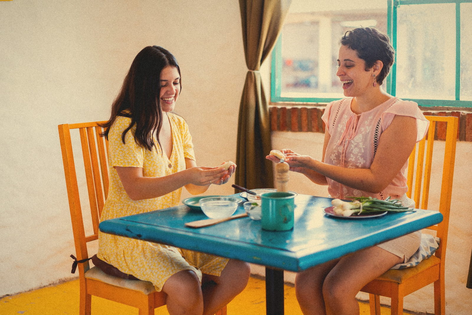 Two friends laughing together at a blue kitchen table