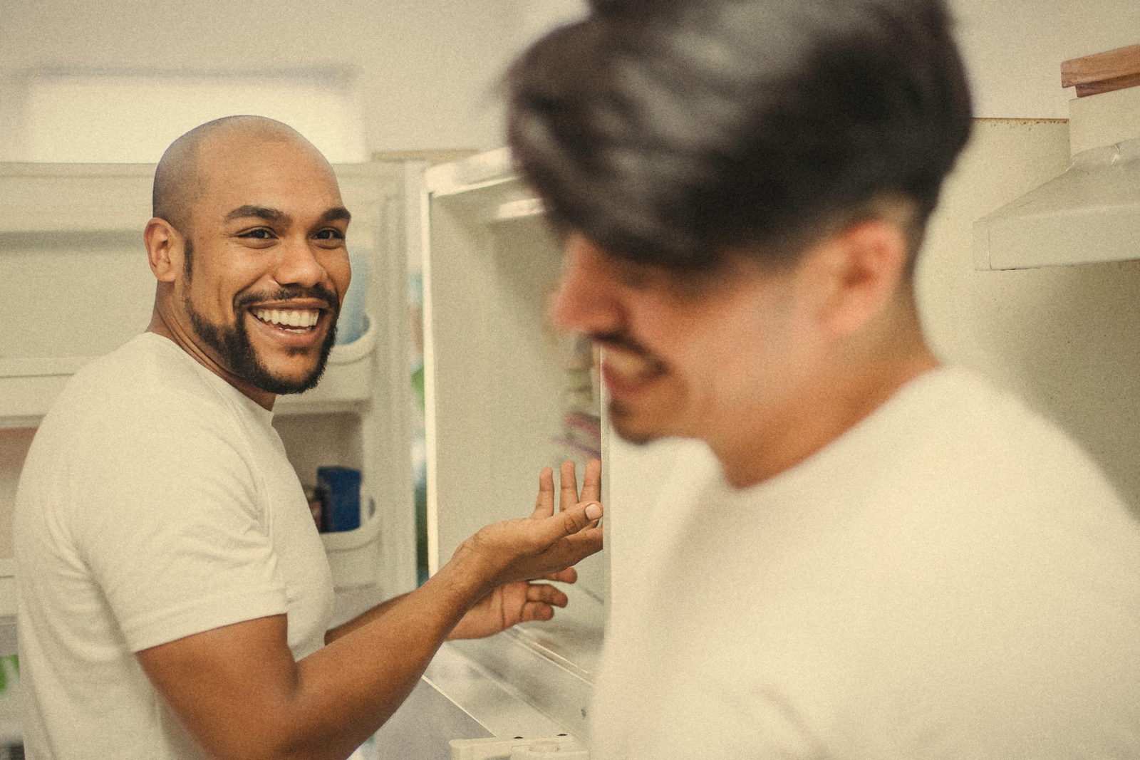 Two friends laughing by the open fridge in a shared kitchen